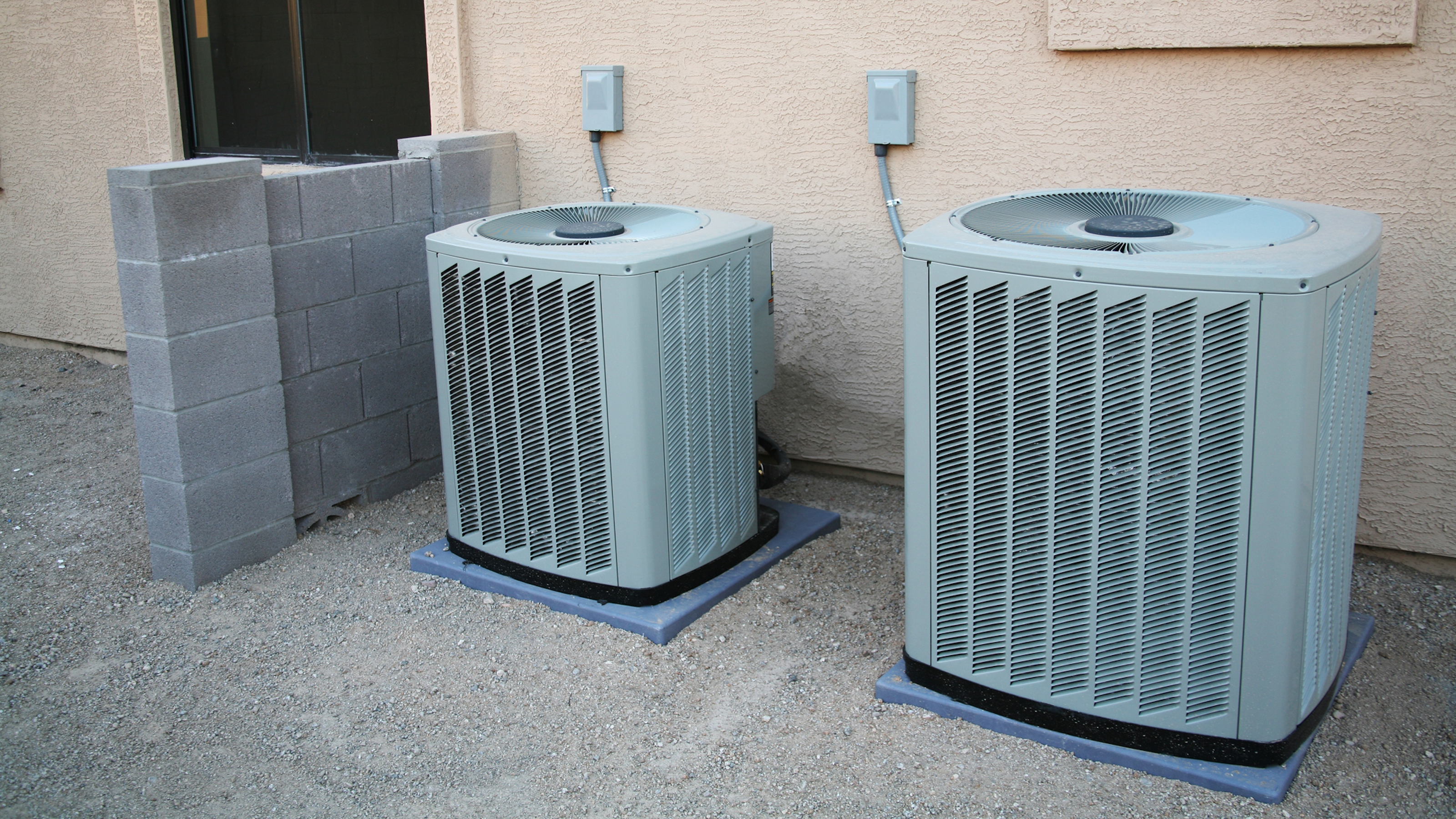 A couple of brand new air conditioners sitting next to a new home. The block wall to the left of them has not been finished yet.